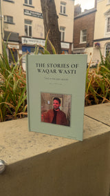 Book titled 'The Stories of Waqar Wasti' on a ledge with a cityscape background